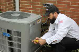 HVAC technician unscrewing side panel of AC unit