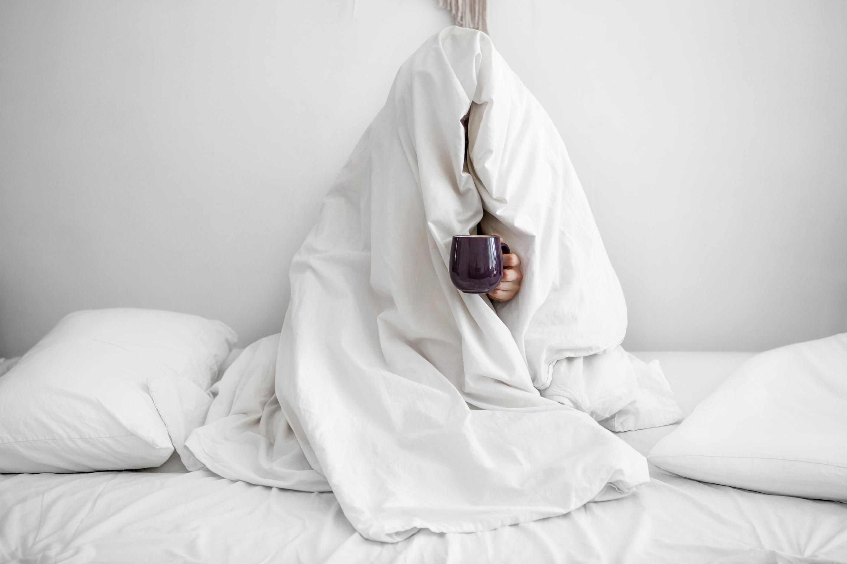 person huddles in comforter holding a mug