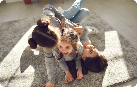 Two children playfully wrestling on a carpeted floor in a sunlit room.
