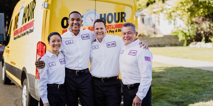 One Hour Heating & Air Conditioning team of technicians smiling and standing together in front of a yellow service van.