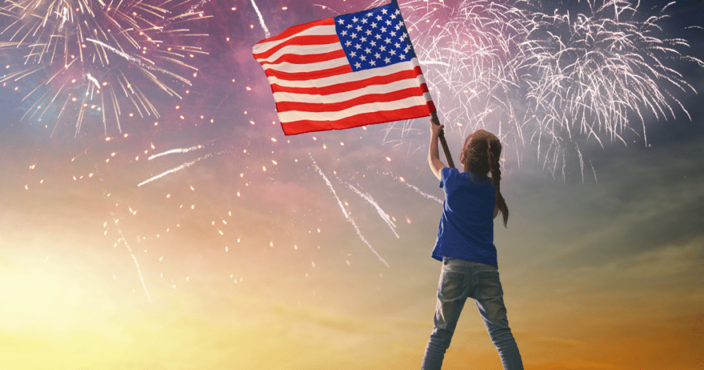 child waving american flag with fireworks behind her