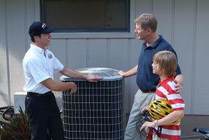 AC technician standing next to AC unit talking to father and son